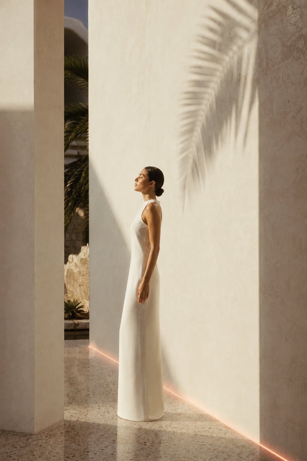 Woman in a white dress standing in a sunlit stucco corridor at golden hour